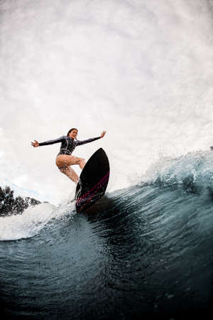 Active woman in black wetsuit professionally rides on surf board on waveの写真素材