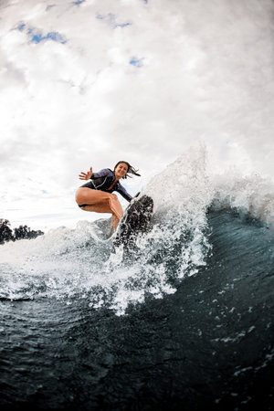 happy woman in wetsuit engaged in extreme sport and rides board on river wave
