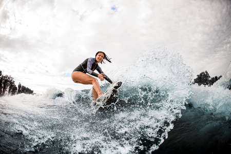 active woman in wetsuit engaged in extreme sport and rides board on river waveの写真素材