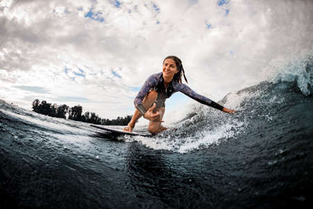 happy woman riding on wave sitting on surf board and touching the water with her hand.の写真素材