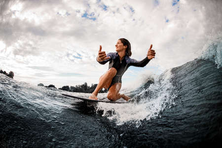 happy woman riding on wave sitting on surf board and shows hand gestureの写真素材
