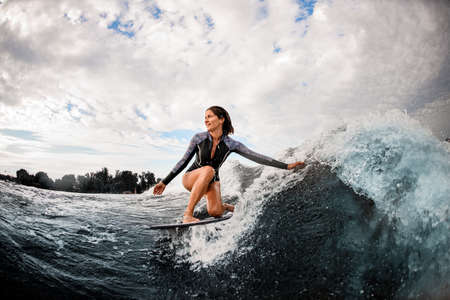 woman having fun sitting on surf board and touching the water with her hand.の写真素材