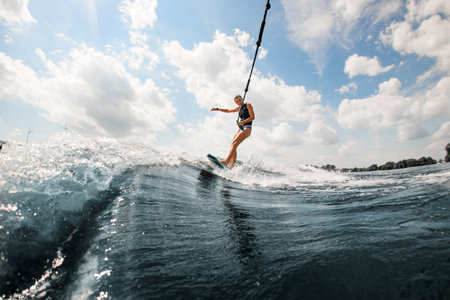 Active young woman riding on the wake surf holding rope of motorboat