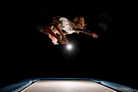 handsome woman beautifully jumps on trampoline in the air at dark timeの写真素材