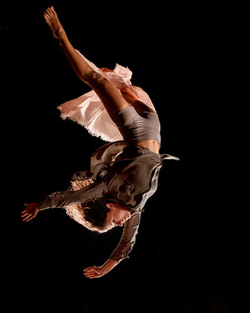 Close-up view of beautiful woman jumps at dark time and performs trick upside down