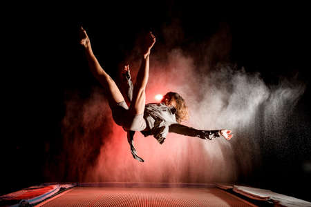 active woman bouncing on trampoline and performs trick in the air at dark timeの写真素材