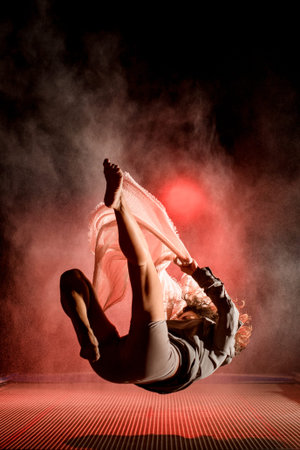 view of athletic woman in the air falling on trampoline in the dark time.