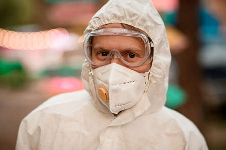Portrait of young man with goggles and respirator and in white protective suitの写真素材
