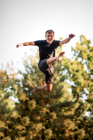 cheerful young man jumps in the air against the background of green trees.