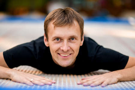 Portrait of young smiling guy in black clothes lying on trampoline.の写真素材