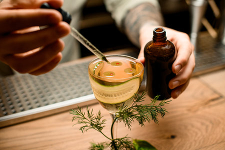 view of man who holds dropper with liquid and carefully adds it to glass with cocktail