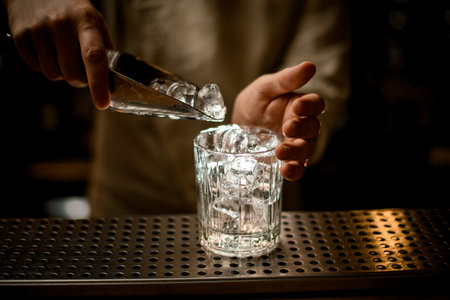 barman holds metal scoop with ice cubes and pours them into old fashioned glassの写真素材