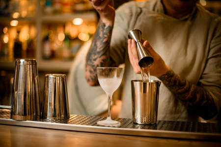 view on bar counter behind which bartender pours liquid from jigger into measuring cup.の写真素材
