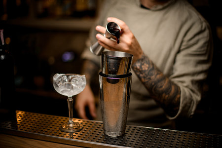 man at bar masterfully pours drink from metal jigger into shaker
