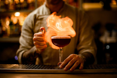 professional bartender sets to fire on wine glass with foam cocktail on bar counter