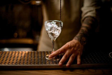 close-up of glass with ice cubes being stirred by bartender with long bar spoonの写真素材