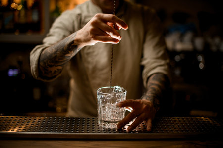 bartender with long bar spoon stir the ice cubes in old fashioned glass