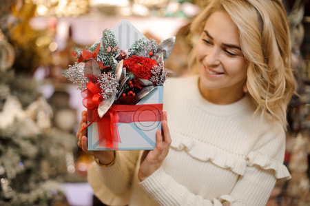 Beautiful christmas composition in square box decorated with ribbon in hands of young blonde woman.