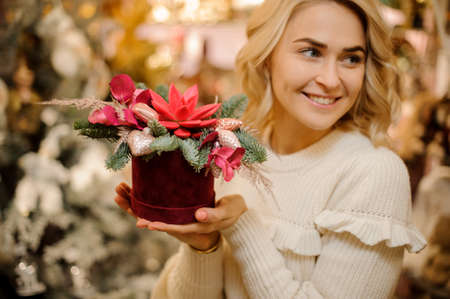 Bright creative flower arrangement decorated with golden Christmas tree decorations in hands of smiling womanの写真素材