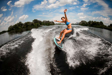 Active athletic woman balancing on the wake board on high wave of motorboatの写真素材