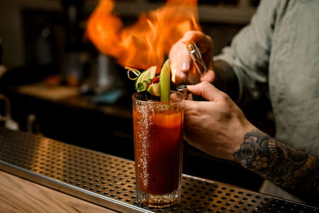 view on bartender who sets fire to glass of cocktail garnished with slices of vegetables.の写真素材