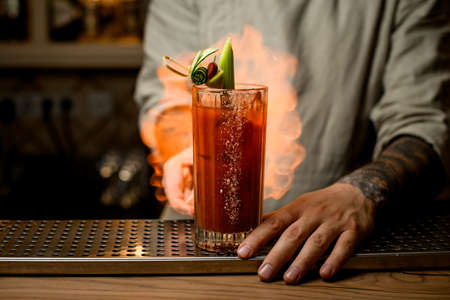 man sets fire to glass of tomato juice cocktail garnished with slices of vegetables.の写真素材