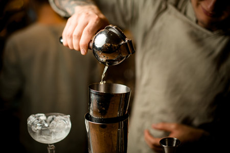 Male barman holds steel squeezer and masterfully squeezes juice into shaker