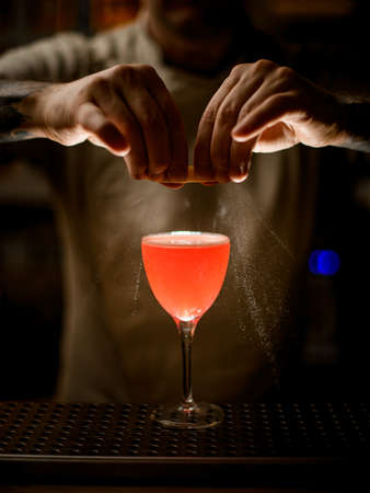 Close-up view of bartender holding lemon peel and skillfully sprinkles on glass with bright cocktail.の写真素材