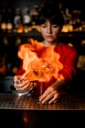 crystal wine glass with alcoholic drink engulfed in fiery flame that stands on the barの写真素材