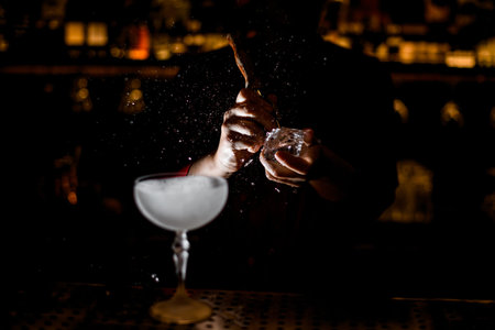 view on hands of bartender who splits ice cube with tool at dark bar