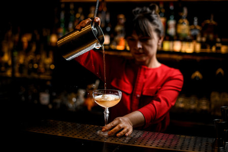 view of shiny glass with cold alcoholic cocktail in which female bartender carefully pours drink
