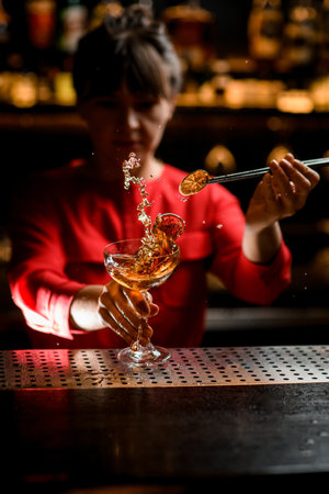 view on bartender womans hand holding glass of splashing drink and decorates itの写真素材