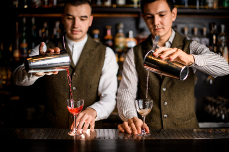two bartenders carefully pour cocktails into glassesの写真素材