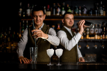 view of bar with glasses full of ice and male bartenders preparing cocktail