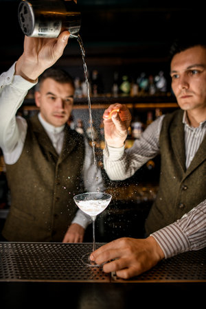 man bartender pours liquid into glass of drink and another man sprinkles on itの写真素材