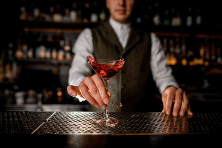 beautiful glass with splashing drink on bar and hand of man bartender holds itの写真素材