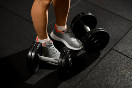 focus on two dumbbells lying on the gym floor near female legsの写真素材
