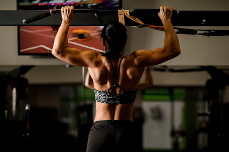 Close-up view of muscular woman doing pull ups in gym. Bodybuilding concept.