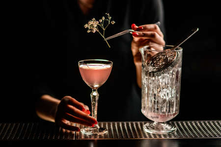 close-up of glass with pink alcoholic drink which woman decorates with sprig of white flowerの写真素材