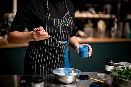 Close-up view of woman chef holding spoon with blue powder and pouring it into bowl