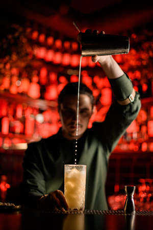 male bartender gently pours cocktail from shaker into glass on the bar counterの写真素材