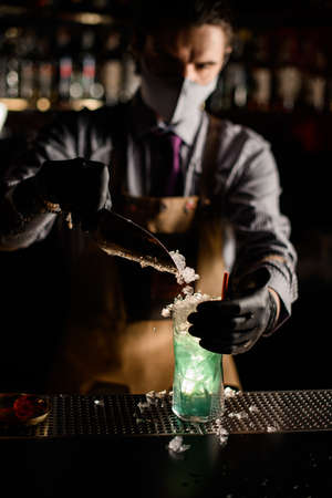 man bartender gently pours ice into glass with cocktail on the barの写真素材