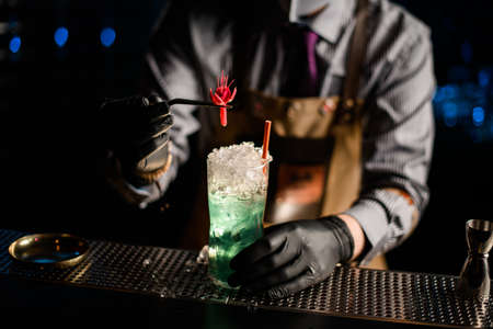 view of glass with cocktail that male bartender decorates with flower using tweezersの写真素材