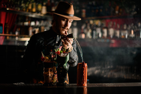 stylish bartender pours liquid into one of the fancy glasses on bar