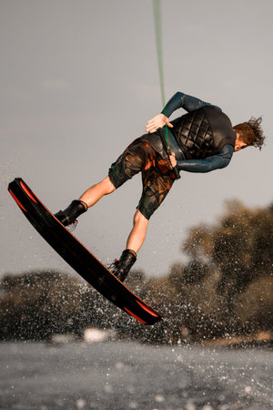 rear view of athletic guy actively jumps on wakeboard holding rope in his hand.