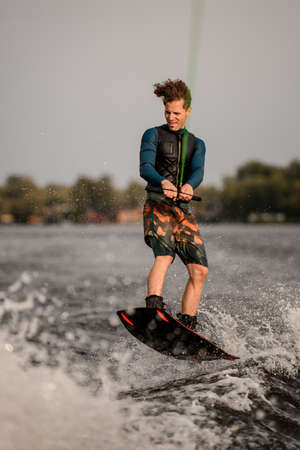 young guy wakeboarder holds rope in his hands and jumping on waveの写真素材