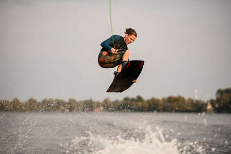 young energetic wakeboarder jumping high over river waterの写真素材