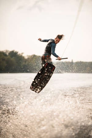 young athletic man jumps spectacularly on wakeboard above the water with splashesの写真素材