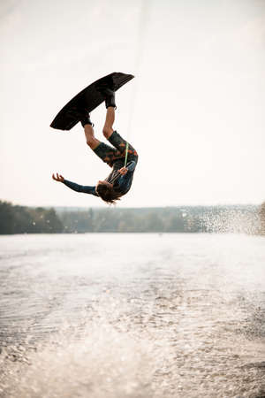 Young athletic man having fun on wakeboard masterfully jumps over splashing river waterの写真素材