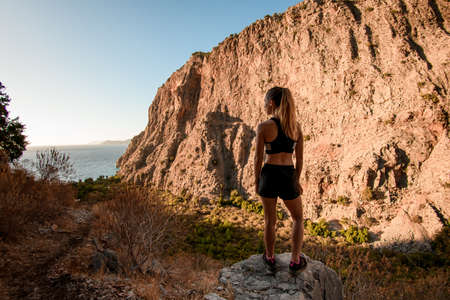 rear view of attractive woman standing on stone and enjoying on view of mountain landscape.の写真素材